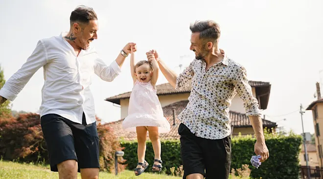 two gay dads having fun with their daughter outside during the summer time