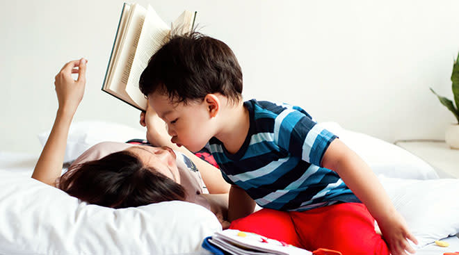 toddler kissing mother while reading books in bed at home