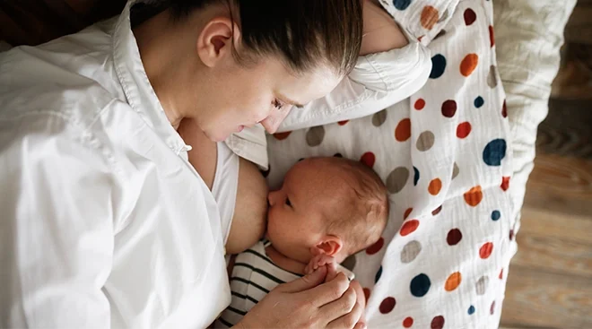 mother breastfeeding baby while lying in bed