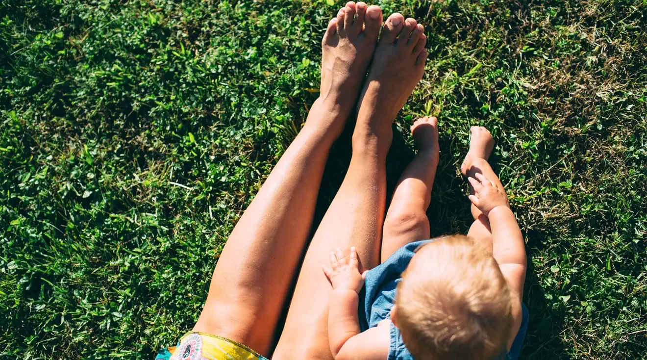 mother and baby sitting on grass outside on a sunny day