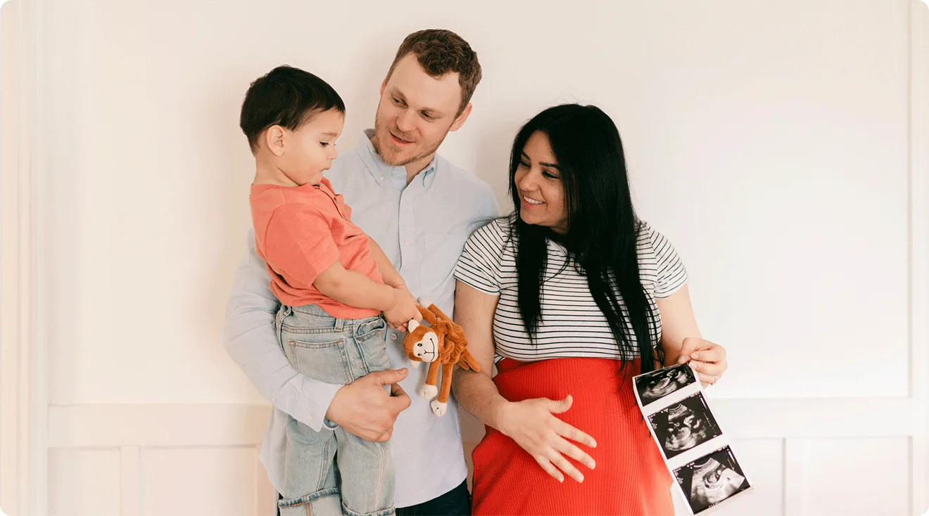 parents with toddler holding ultrasound photos pregnancy announcement