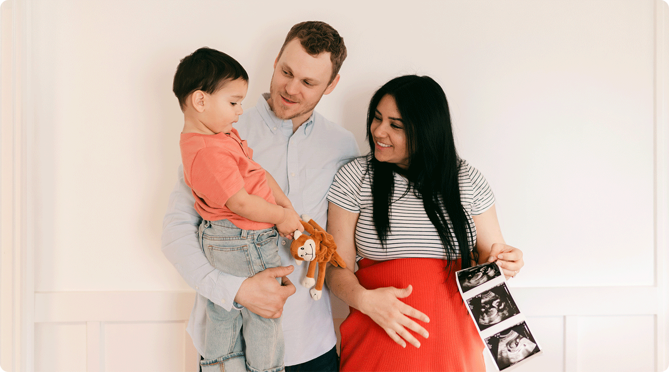 parents with toddler holding ultrasound photos pregnancy announcement 