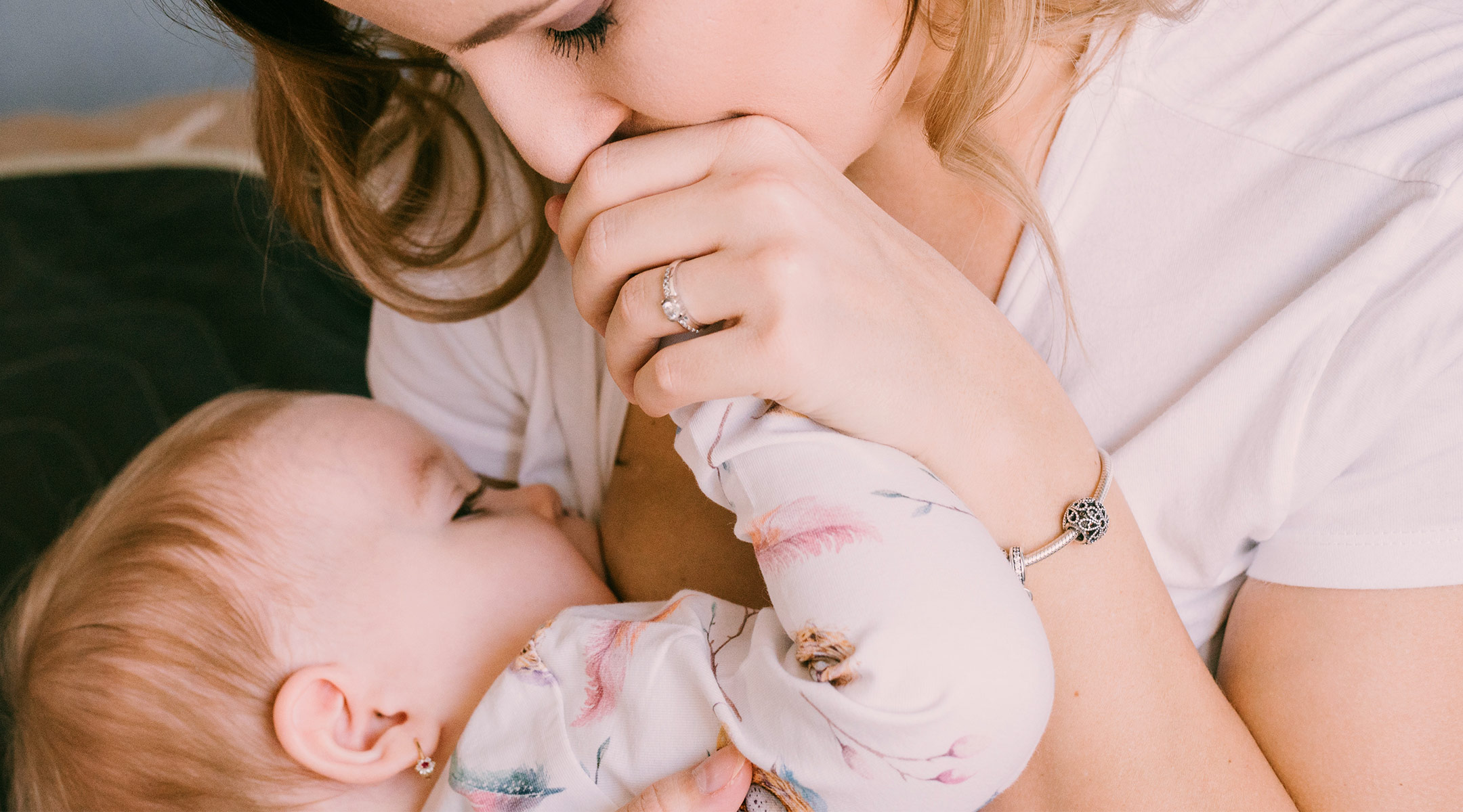 tender moment of mom breastfeeding baby while kissing her hand