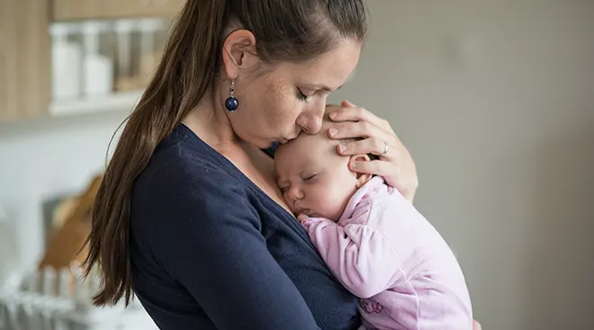 mother holding and kissing newborn baby at home