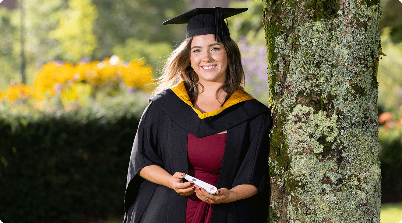 Leah Shanahan in graduation cap and gown with pregnancy test for the blind