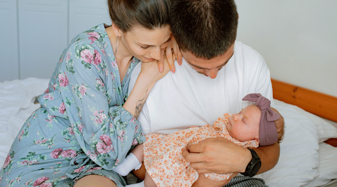 dad holding newborn baby next to mom at home