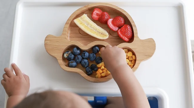 overhead view of baby sitting at high chair and eating food with fingers