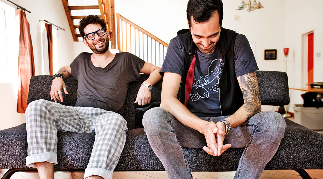 two men sitting on couch at home laughing