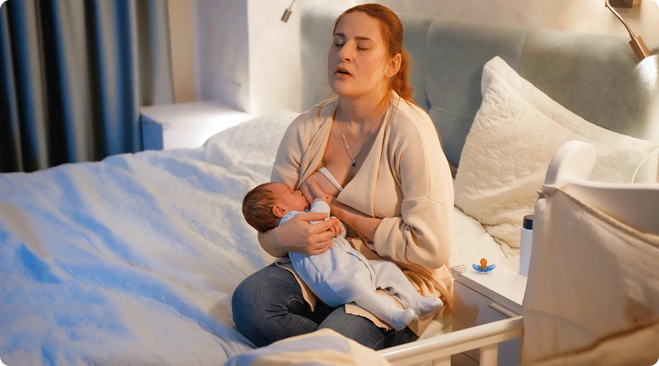 tired mom breastfeeding newborn baby in bedroom