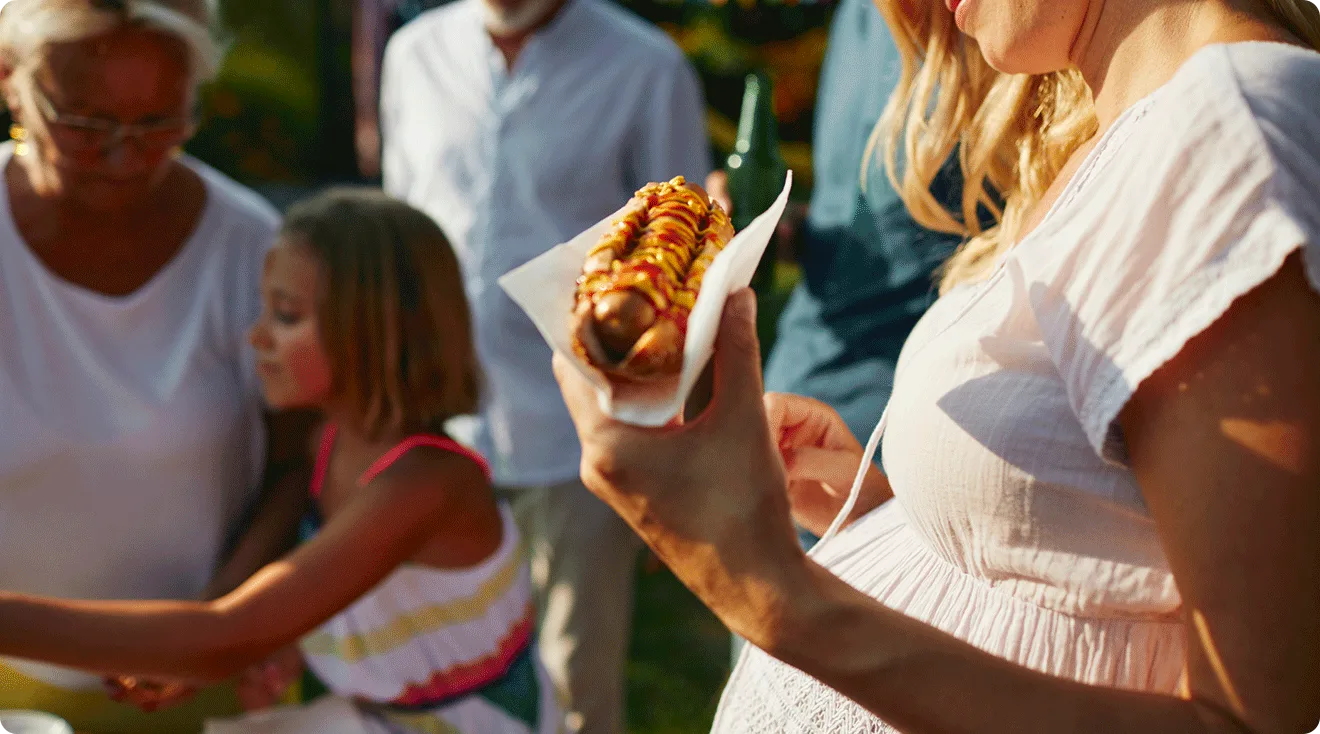 pregnant woman holding a hot dog at a summer barbecue party