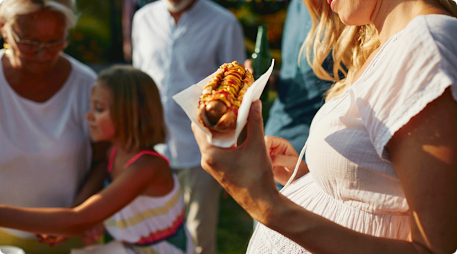 pregnant woman holding a hot dog at a summer barbecue party