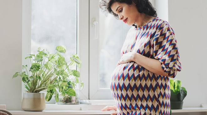 pensive pregnant woman looking down by sunny window