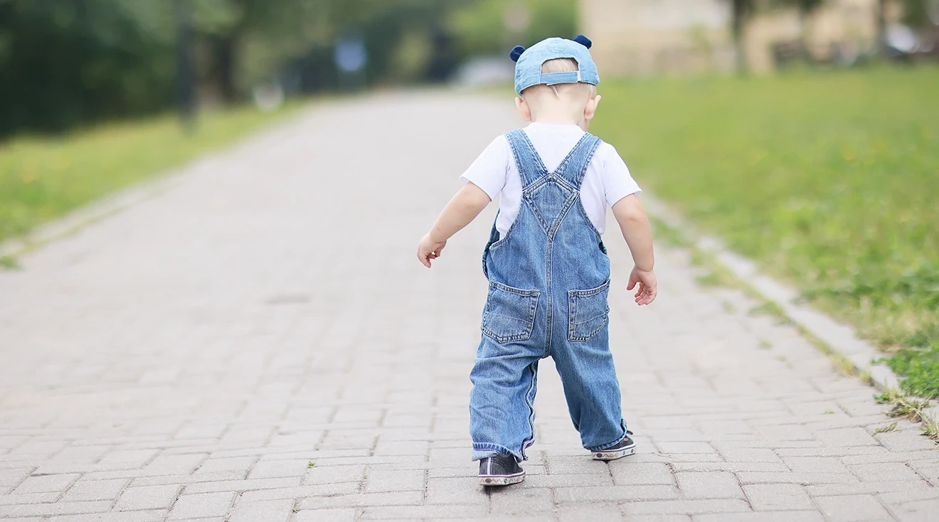 baby walking outside wearing denim overalls and sneakers