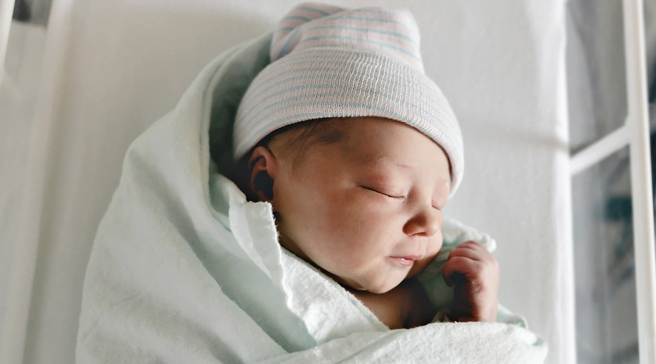 swaddled newborn baby in hospital bed