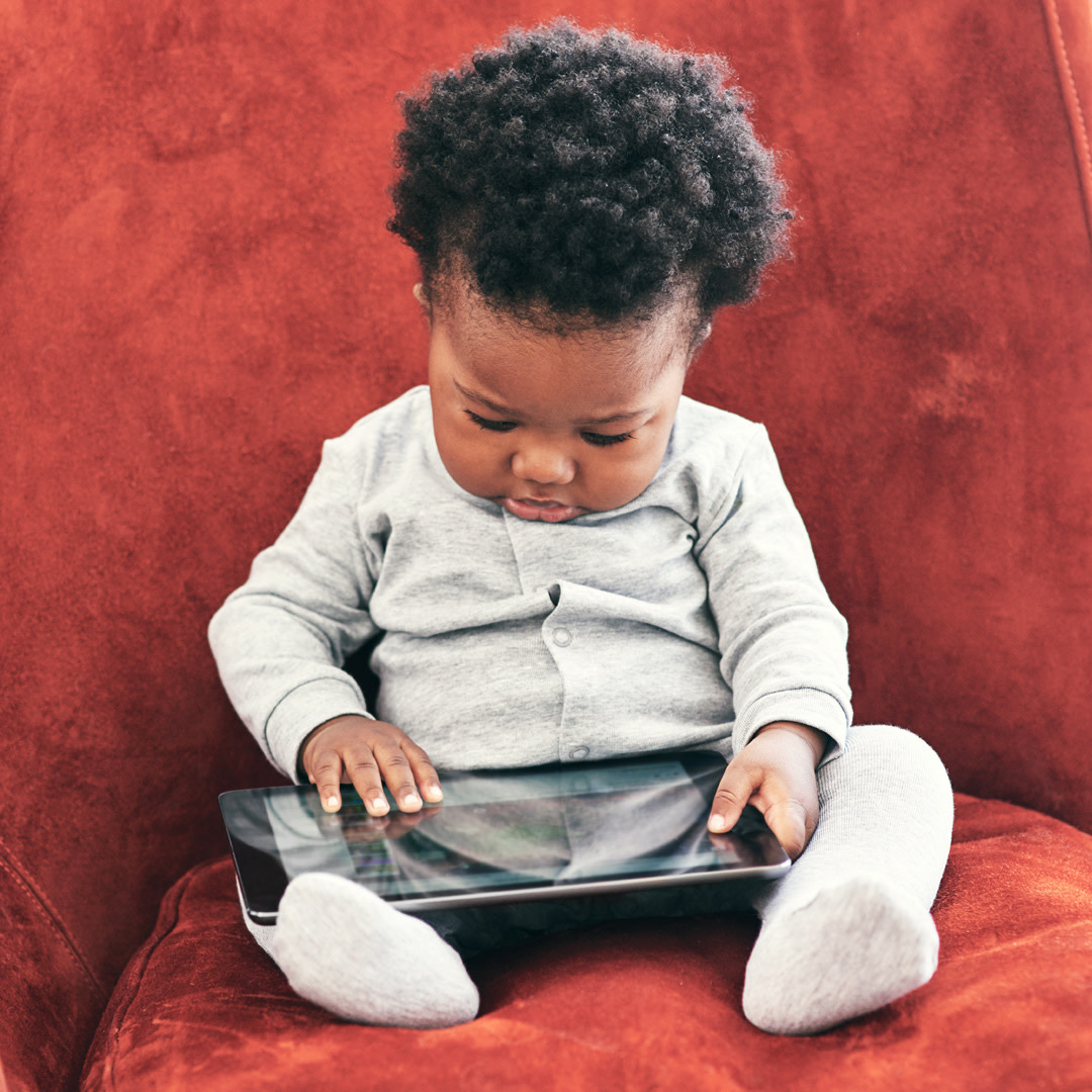 Baby sits in chair while playing on iPad