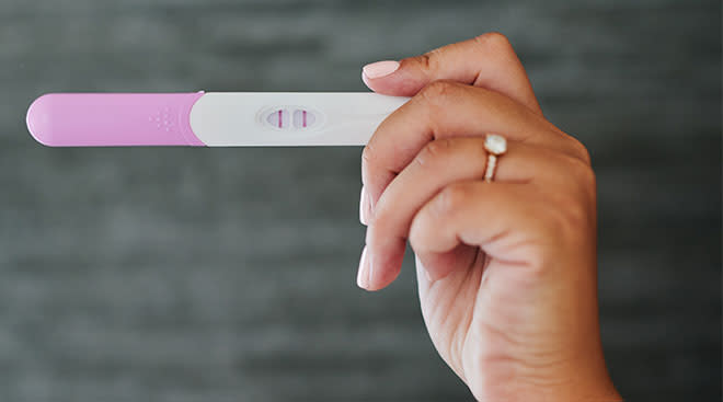 Close up of woman's hand holding a positive pregnancy test.