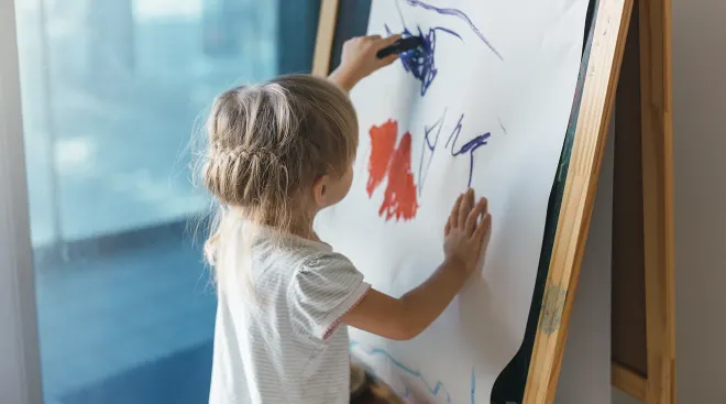 toddler girl drawing on easel at home