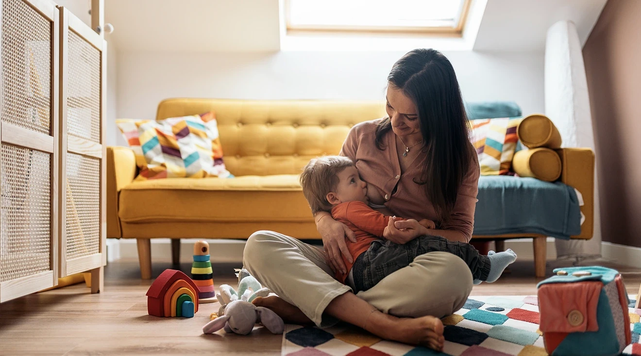 mother breastfeeding toddler in playroom at home