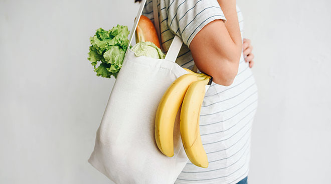 pregnant woman holding reusable bag with fruits and vegetables