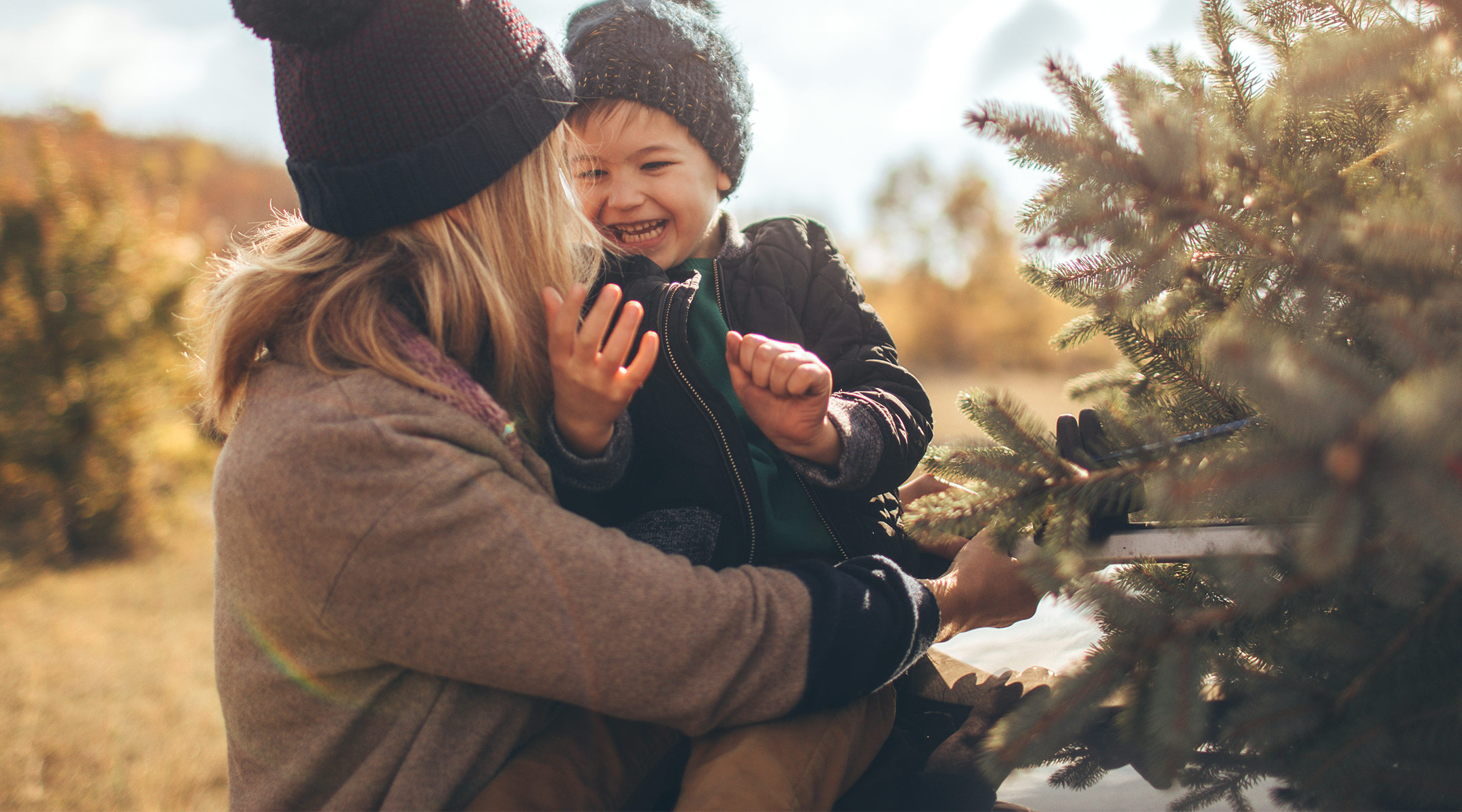 mom holding her young son while getting their christmas tree ready