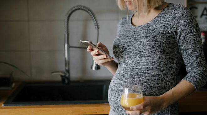 pregnant woman standing in kitchen and looking at phone