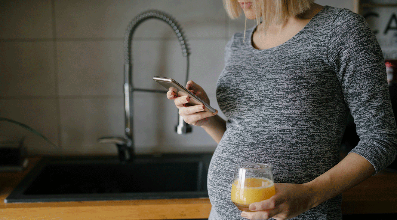 pregnant woman standing in kitchen and looking at phone