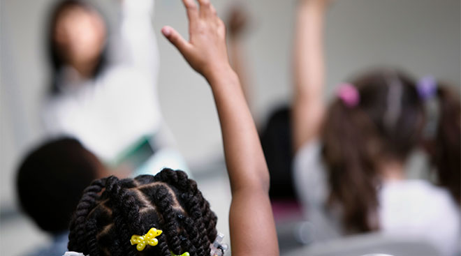 children in classroom with their hands raised