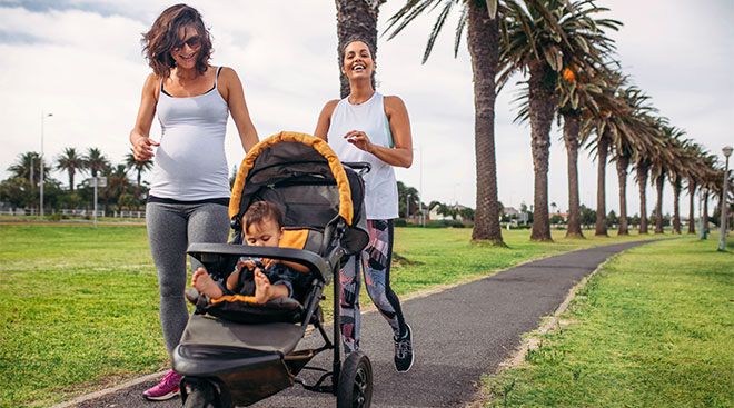 Pregnant woman and her friend walking with baby in stroller for exercise. 