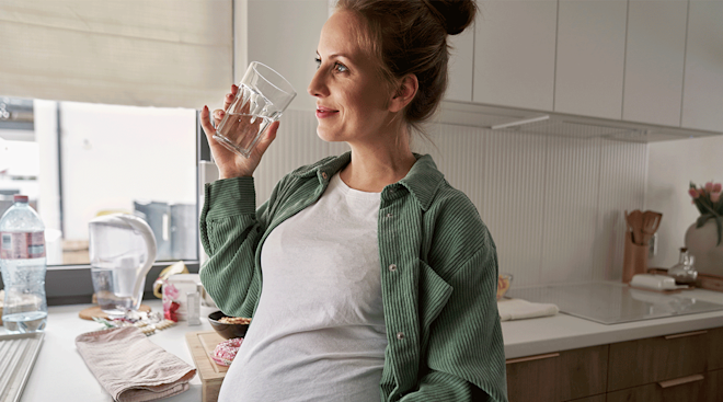 pregnant woman drinking water in kitchen at home