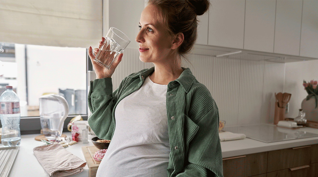 pregnant woman drinking water in kitchen at home