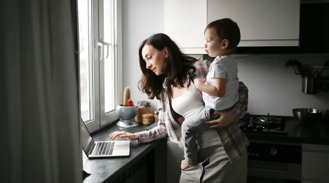 mother holding baby while shopping online in kitchen at home