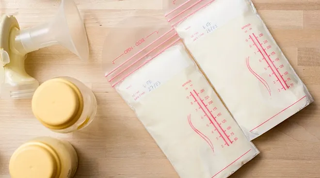breast milk in bags next to breast pump and bottles on wood table
