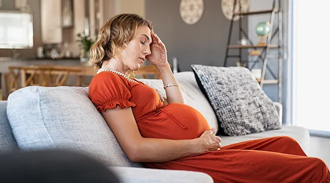 young pregnant woman feeling sick while sitting on couch at home