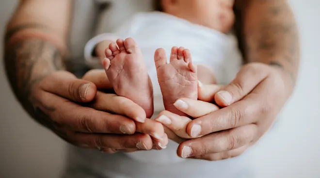 Two parents holding newborn's feet