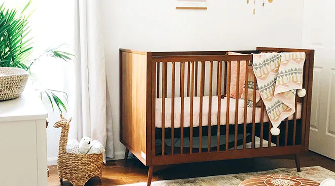 baby nursery with a medium hued wooden crib and blanket draped over the side