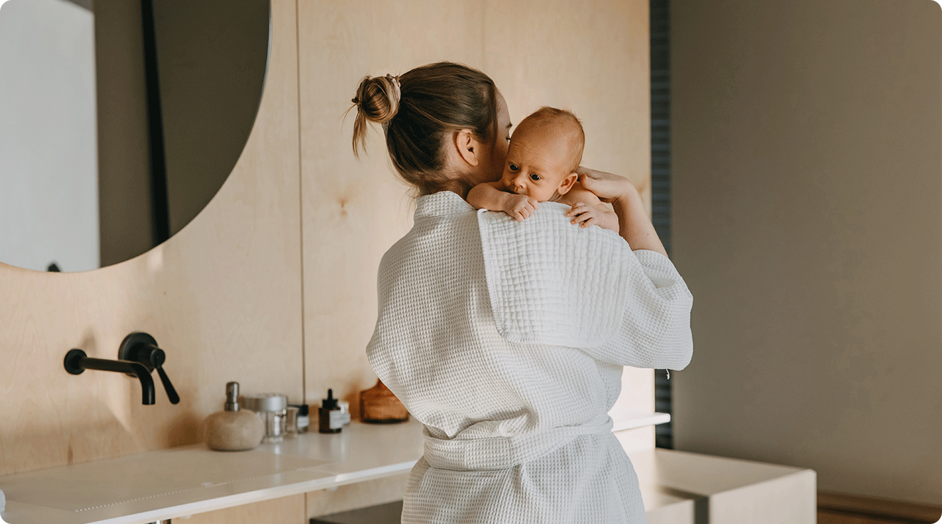 postpartum mom wearing a robe while holding newborn in bathroom at home