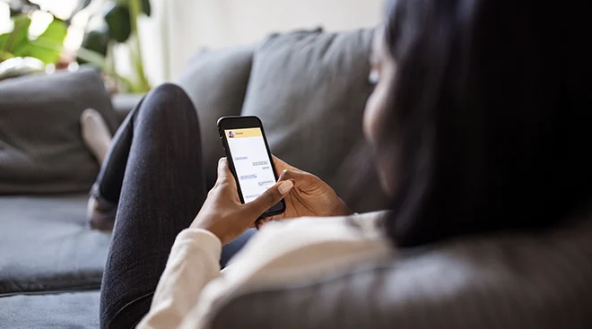 young woman using dating app on smartphone while sitting on couch at home