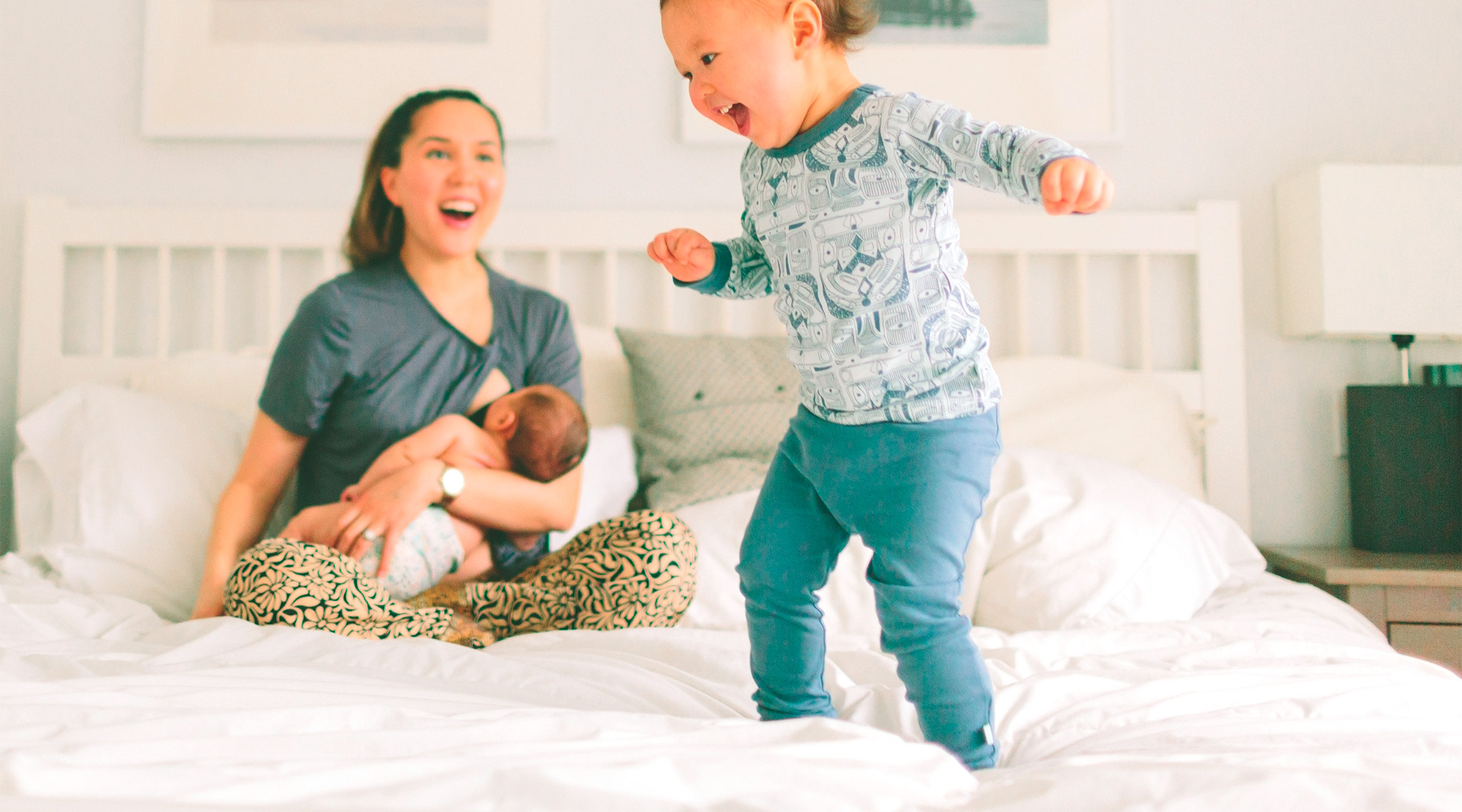 mom breastfeeding baby and happily watching her toddler at home.