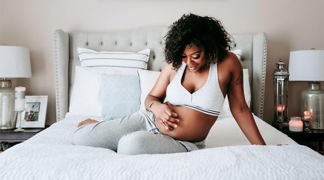 pregnant woman hanging out on her bed and laughing in maternity bra