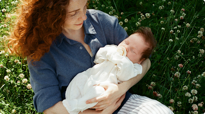 A mom holding her newborn baby outside in a flower field.