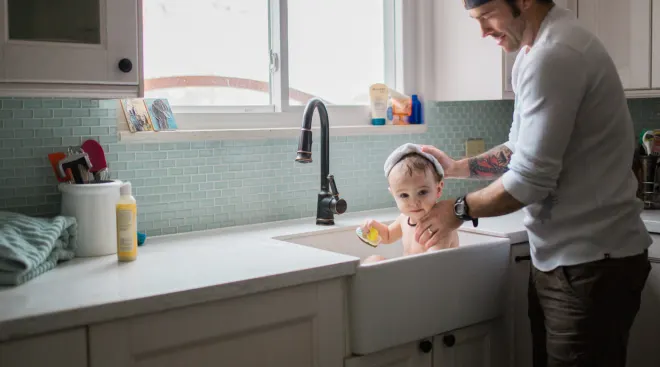 Dad giving baby a bath in the kitchen sink. 