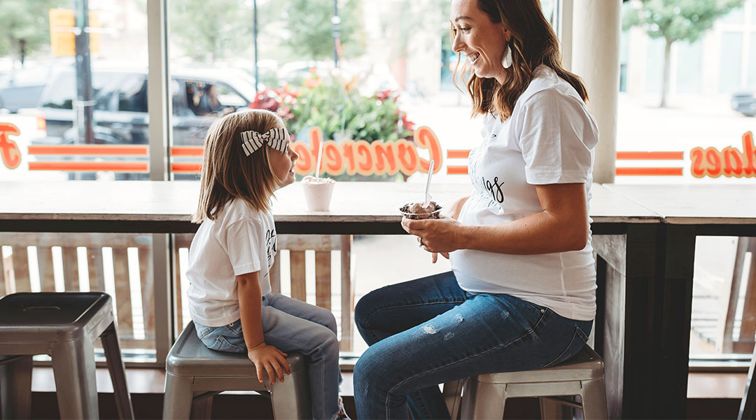 Pregnant mom sits with her young daughter eating ice cream