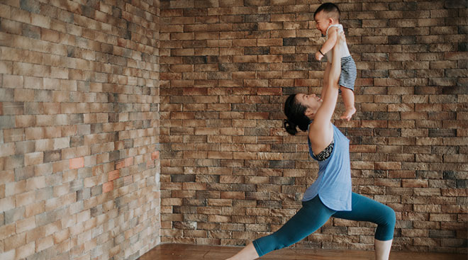 Woman exercising at home while holding her baby up.