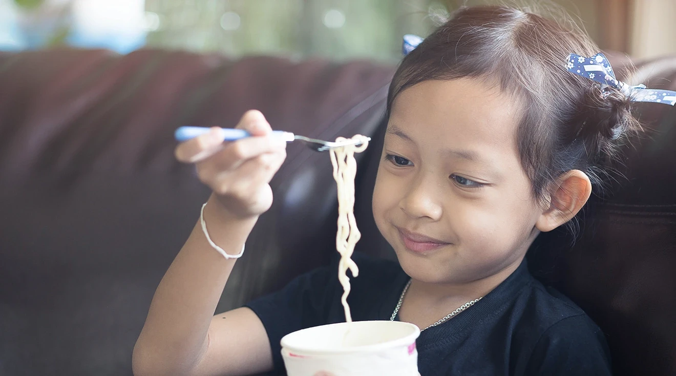young girl eating noodles on the couch at home