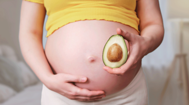 pregnant woman holding a sliced avocado