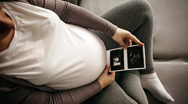 woman holding photo of ultrasound while sitting on couch at home