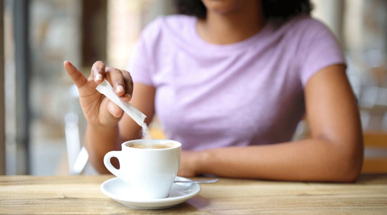 woman pouring sugar packet into coffee cup