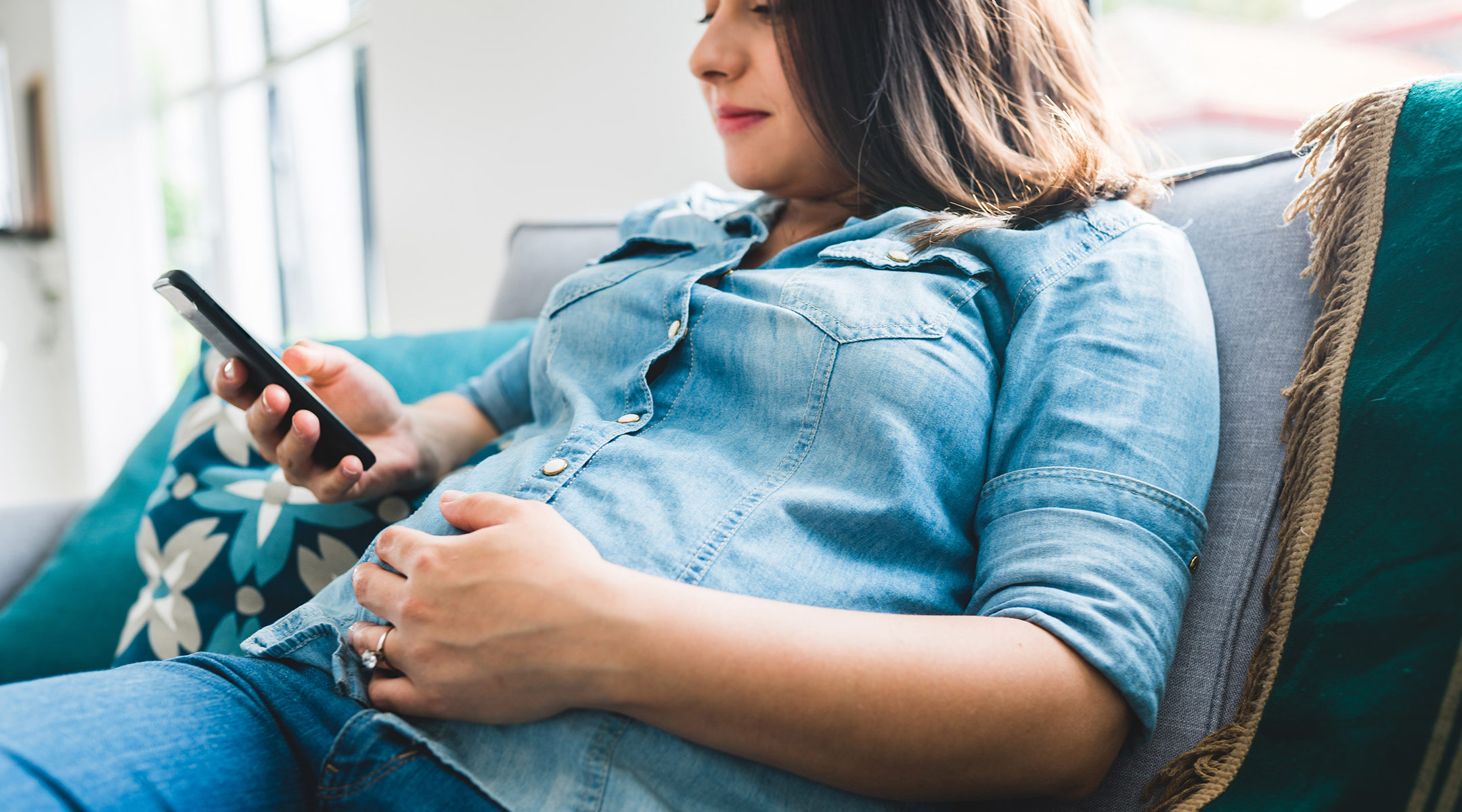 pregnant woman sits on the couch and looks at phone