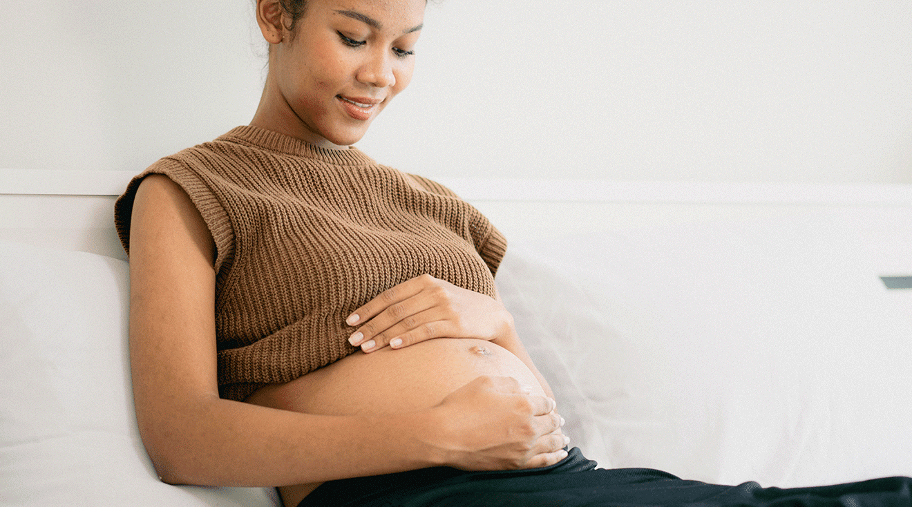 pregnant woman holding belly while sitting on couch at home