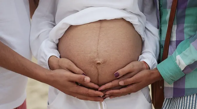 two people touching a pregnant belly, surrogacy concept